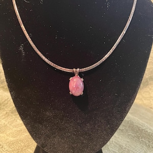 May include: A silver chain necklace with a pink oval pendant. The pendant has a silver setting and a pink stone.