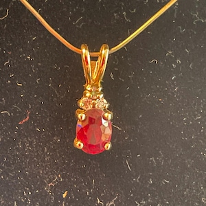 May include: A gold pendant necklace with a red oval gemstone and two smaller clear gemstones.