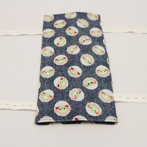 May include: A rectangular, dark blue fabric item with a repeating pattern of green-skinned, large-eyed characters in white circles. White elastic bands extend from the sides. The item appears to be a case or cover.