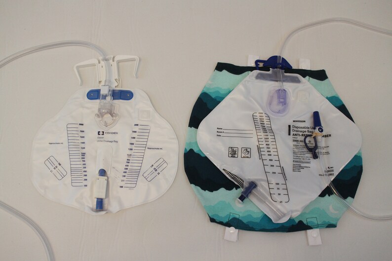 May include: Two disposable urine drainage bags. One is white with a clear tube and a scale printed on the front. The other is white with a blue and green patterned backing and a clear tube. Both have measurement scales.