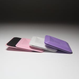 K&ouml;nnte beinhalten: Drei quadratische, strukturierte, selbstklebende Pads in Schwarz, Rosa und Lila.