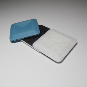 K&ouml;nnte beinhalten: Zwei quadratische Untersetzer, einer blau und einer wei&szlig; mit einem gesprenkelten Muster. Die Untersetzer sind aus einem strukturierten Material.