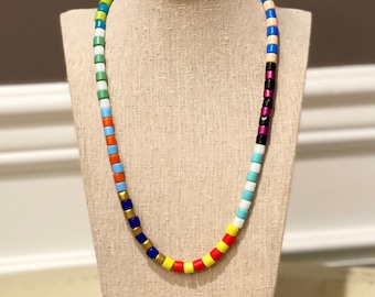Op de afbeelding: Een kleurrijke kralenketting met afwisselende kleuren rood, oranje, geel, groen, blauw en wit. De ketting is op een beige mannequin.