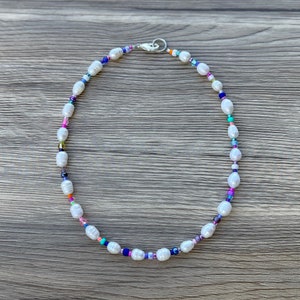 May include: A white pearl necklace with colourful beads. The necklace is on a wooden surface.