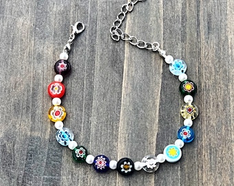 Peut inclure: Un bracelet coloré avec des perles de perles blanches et des breloques de fleurs en verre. Le bracelet a un fermoir argenté.