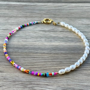 May include: A colorful beaded necklace with a single strand of white pearls. The necklace is made with small, colorful beads and has a gold clasp.