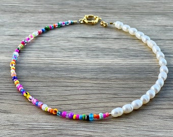May include: A colourful beaded necklace with a single strand of white pearls. The necklace is made with small, colourful beads and has a gold clasp.