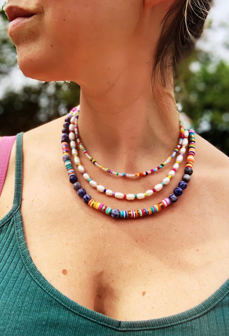 May include: A layered necklace with colorful beads and white pearls. The necklace is made of different materials, including wood, glass, and metal. The necklace is a statement piece and would be perfect for a casual or formal occasion.