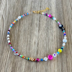 Op de afbeelding: Een kleurrijke kralenketting met verschillende bedels, waaronder harten, smiley-gezichten en een yin-yang symbool. De ketting is gemaakt met witte, roze, blauwe, gele, groene en rode kralen.