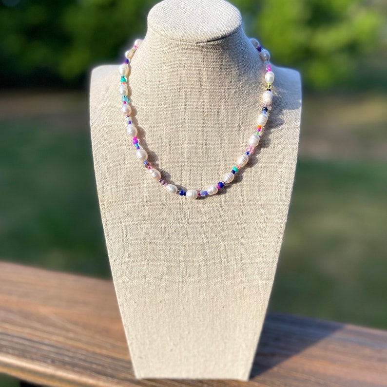 May include: A white pearl necklace with colourful beads. The necklace is on a white mannequin bust.
