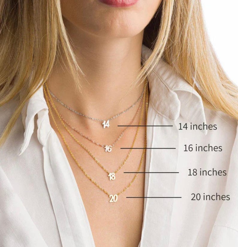 May include: Four gold necklaces with numbers 14, 16, 18, and 20 on them. The necklaces are layered on a model wearing a white shirt. The numbers indicate the length of each necklace in inches.