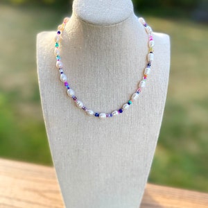 May include: A white pearl necklace with colourful beads. The necklace is on a white mannequin bust.