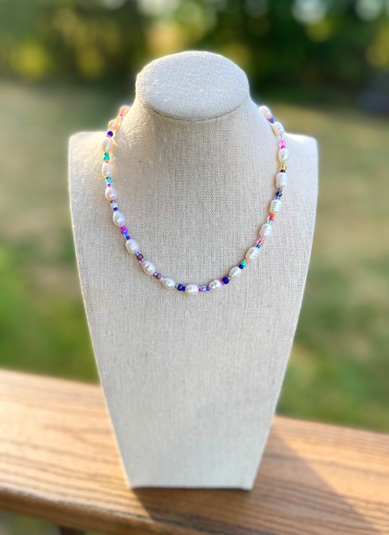 May include: A white pearl necklace with colourful beads. The necklace is on a white mannequin bust.