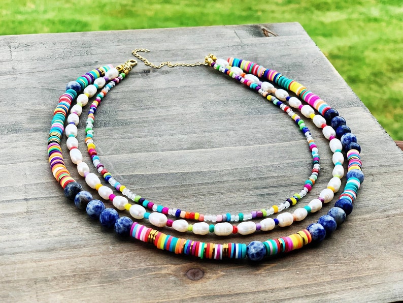 May include: A multi-layered necklace with white pearls, blue lapis lazuli beads, and colorful round beads. The necklace is made of different materials and has a bohemian style.