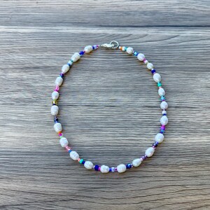 May include: A white pearl necklace with colourful beads. The necklace is on a wooden surface.