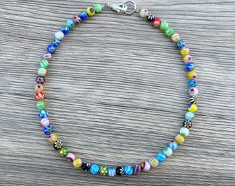 May include: A vibrant beaded necklace with small, round beads in various colours, including blue, green, yellow, red, and white. The beads are strung together with a silver-coloured clasp. The necklace is approximately 40 cm long.
