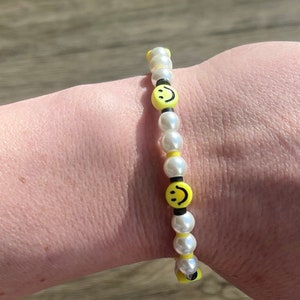 Könnte beinhalten: Ein weißes Perlenarmband mit gelben Smiley-Perlen.