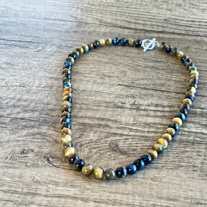 May include: A necklace made of blue and gold tiger's eye beads with a silver toggle clasp.