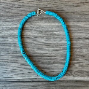 May include: A turquoise blue beaded necklace with a silver clasp.