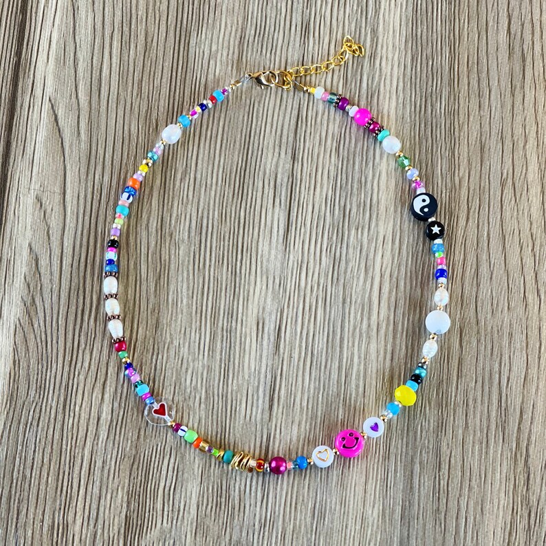 Op de afbeelding: Een kleurrijke kralenketting met verschillende bedels, waaronder een hart, een smiley en een yin yang symbool.