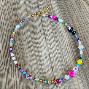 Op de afbeelding: Een kleurrijke kralenketting met verschillende bedels, waaronder een yin yang symbool, een hartje en een smiley. De ketting is gemaakt van witte, roze, blauwe, groene, gele en zwarte kralen.