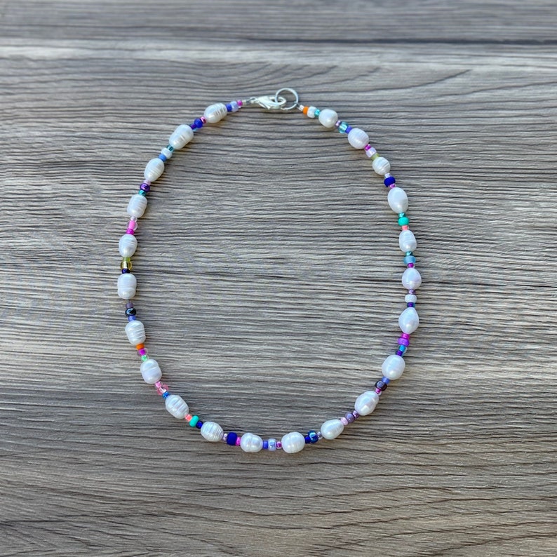 May include: A white pearl necklace with colourful beads. The necklace is on a wooden surface.