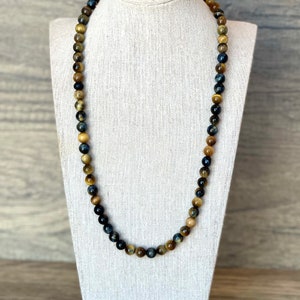 May include: A long necklace made of blue, gold, and brown tiger's eye beads.
