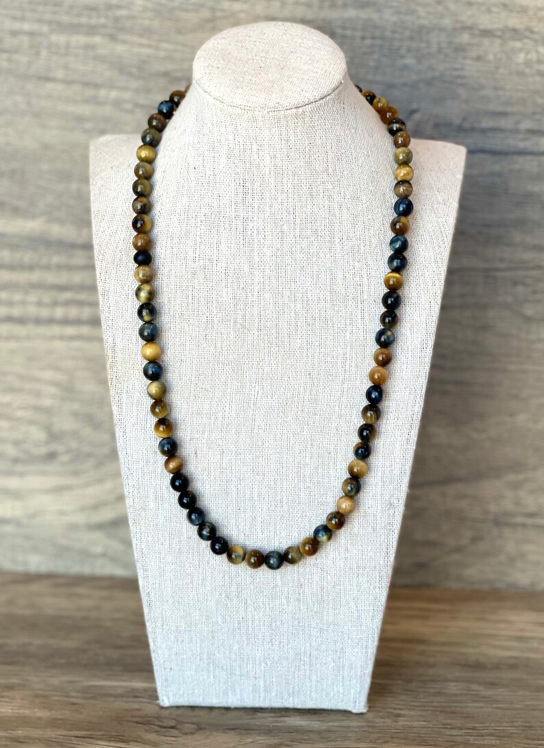May include: A long necklace made of blue, gold, and brown tiger's eye beads.