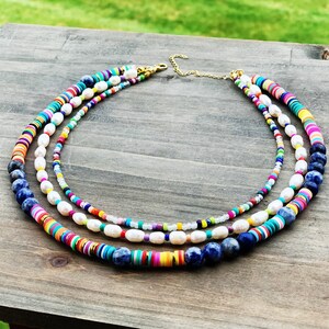 May include: A multi-layered necklace with colorful beads, white pearls, and blue lapis lazuli stones. The necklace is made of different materials and has a bohemian style.