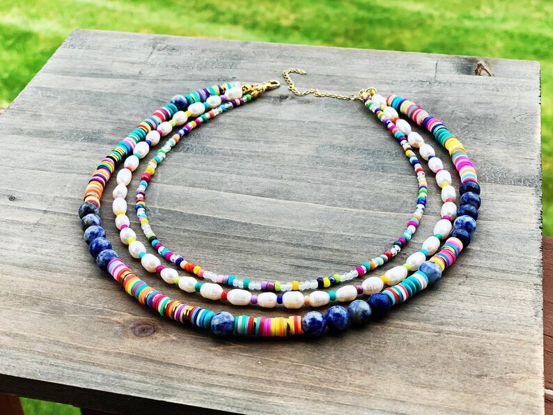 May include: A multi-layered necklace with colorful beads, white pearls, and blue lapis lazuli stones. The necklace is made of different materials and has a bohemian style.