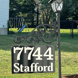 Puede incluir: Se&ntilde;al de n&uacute;mero de casa de metal negro con n&uacute;meros y texto blancos. La se&ntilde;al dice "7744 Stafford". La se&ntilde;al est&aacute; unida a un poste de metal negro con un dise&ntilde;o decorativo de rosas.
