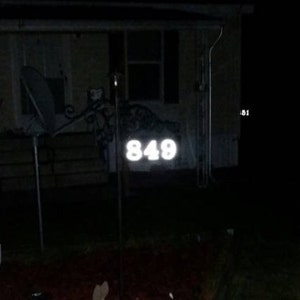 Puede incluir: Primer plano de un letrero de n&uacute;mero de casa con el n&uacute;mero 849 iluminado en blanco sobre un fondo oscuro.
