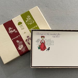 May include: A rectangular stationery box with a cream lid featuring a maroon stripe with white illustrations of a carriage and roses, and a green stripe with a lamp and figure. Inside, a note card displays a person with a poodle and the text Always in the market for NEWS.