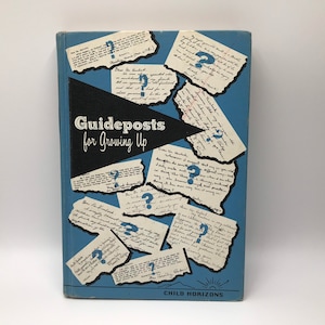 May include: A blue book cover with the title "Guideposts for Growing Up" in white text. The cover features a design of question marks on white paper scraps.