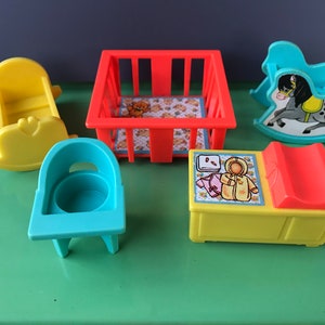 May include: A set of five plastic toys for a baby's nursery, including a yellow rocking cradle, a blue high chair, a red crib, a yellow changing table with a red changing pad, and a blue rocking horse.