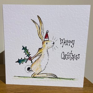 Tarjeta navideña ilustrada a mano con un conejo, una liebre y un acebo de color marrón nuez. Se puede personalizar.