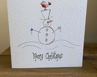 Tarjeta navideña con muñeco de nieve dibujado a mano y petirrojo. Se puede personalizar.