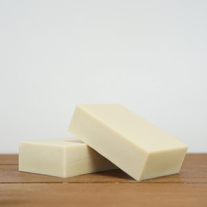 May include: Two rectangular bars of ivory-coloured soap stacked on top of each other on a wooden surface.