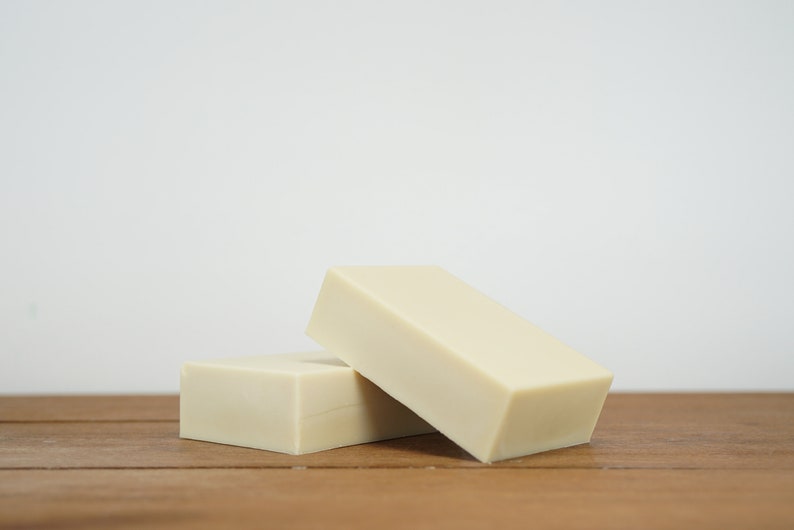 May include: Two rectangular bars of ivory-coloured soap stacked on top of each other on a wooden surface.