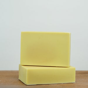 May include: Two bars of pale yellow soap stacked on top of each other on a wooden surface.