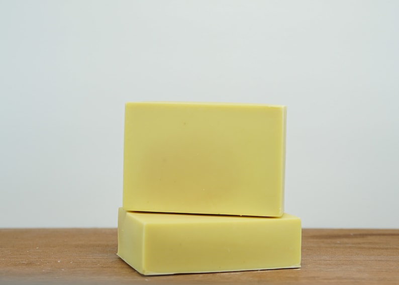 May include: Two bars of pale yellow soap stacked on top of each other on a wooden surface.