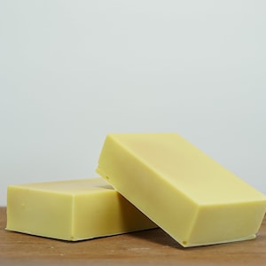 May include: Two rectangular bars of pale yellow soap on a wooden surface.