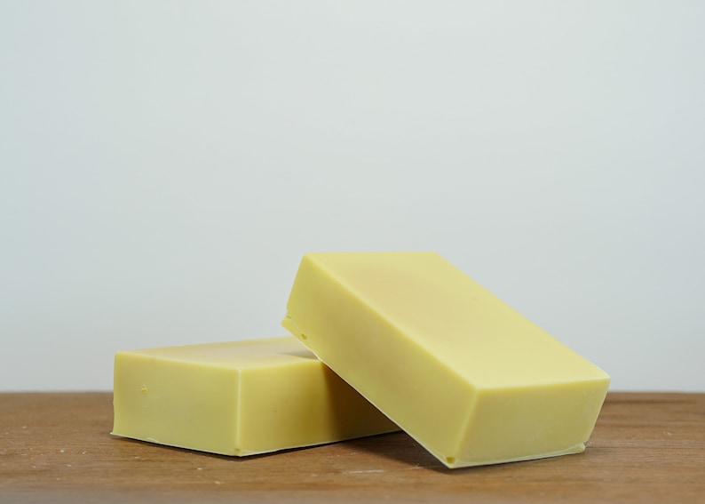 May include: Two rectangular bars of pale yellow soap on a wooden surface.