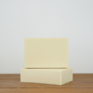 May include: Two rectangular bars of ivory-coloured soap stacked on top of each other on a wooden surface.