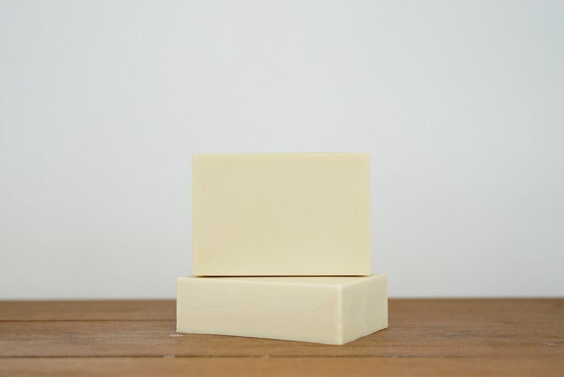 May include: Two rectangular bars of ivory-coloured soap stacked on top of each other on a wooden surface.