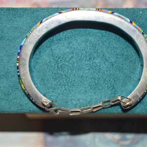 May include: Silver-tone hinged bracelet with colorful mosaic inlay. The mosaic features a pattern of blue, green, yellow, and red accents. The bracelet is connected with a small chain.