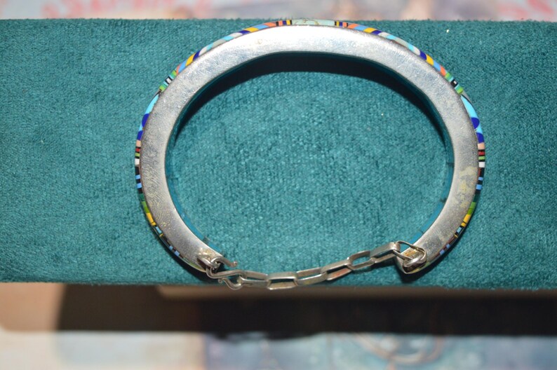 May include: Silver-tone hinged bracelet with colorful mosaic inlay. The mosaic features a pattern of blue, green, yellow, and red accents. The bracelet is connected with a small chain.