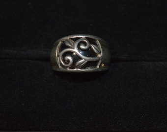 May include: Silver-toned ring with a black inlay and a decorative leaf and swirl design. The ring has a wide band and a detailed, openwork pattern. The ring is set against a dark background.