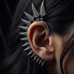 May include: A silver-toned ear cuff featuring a series of articulated fern leaf segments that follow the outer curve of the ear. The metal has a textured, oxidized finish, and the design extends from the upper cartilage down to the earlobe.