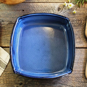 Peut inclure: Un plat à four carré en céramique bleu avec un bord bleu foncé. Le plat est vide et posé sur une surface en bois.